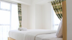 A neatly made bed with white linens, a wooden headboard, and a window with sheer curtains.
