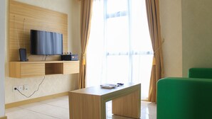 A modern living room with a flat-screen TV mounted on a wooden wall, a green sofa, and a small coffee table.