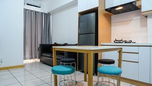 A compact kitchen with a refrigerator, a dining table with stools, and a sofa.