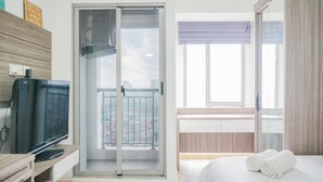 A hotel room with a balcony, a television, a bed with towels, and a sliding door to the balcony. - Strategic Studio Apartment with Extra Bed at M-Town Residence (Gading Serpong)