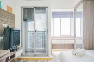 Habitación de hotel con balcón, televisión, cama y toallas, además de una puerta corredera al balcón.