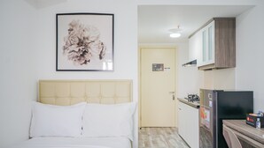 A bedroom with a bed, a framed floral artwork, and a kitchenette with a refrigerator and stove. - Strategic Studio Apartment with Extra Bed at M-Town Residence (Gading Serpong)