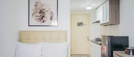 Ein Schlafzimmer mit einem Bett, einer gerahmten Blumenblume und einer Küchenzeile mit Kühlschrank und Herd.
