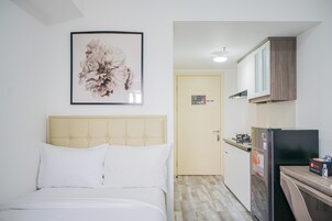 Un dormitorio con cama, una obra de arte floral enmarco y una kitchenette con refrigerador y estufa.