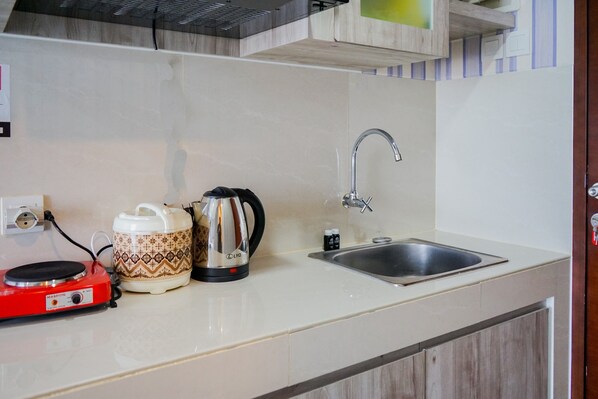 A kitchen with a sink, a red electric stove, a patterned coffee pot, and a kettle.