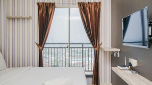 A hotel room with a large bed, a TV mounted on the wall, and a view of the city through the window. - Cozy Living Studio Apartment at Springwood Residence (Tangerang)