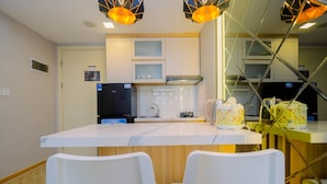 A modern kitchen with white cabinets, a black refrigerator, and a white countertop. There are two white chairs and a yellow chair at the table. - Relax 3BR Apartment at M-Town Residence (Gading Serpong)