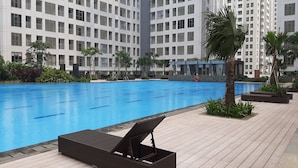 A swimming pool with lounge chairs, surrounded by tall residential buildings. - Relax 3BR Apartment at M-Town Residence (Gading Serpong)