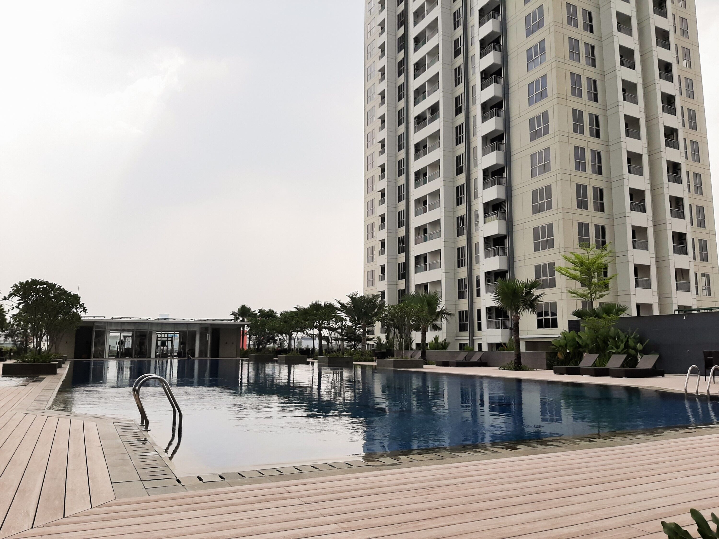 A modern high-rise building with a swimming pool and surrounding greenery.