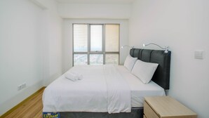 A bedroom with a bed, a nightstand, and a window with blinds. - Brand New 1BR Apartment at M-Town Signature (Gading Serpong)