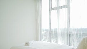 A hotel room with a large window, a neatly made bed, and a view of the cityscape.