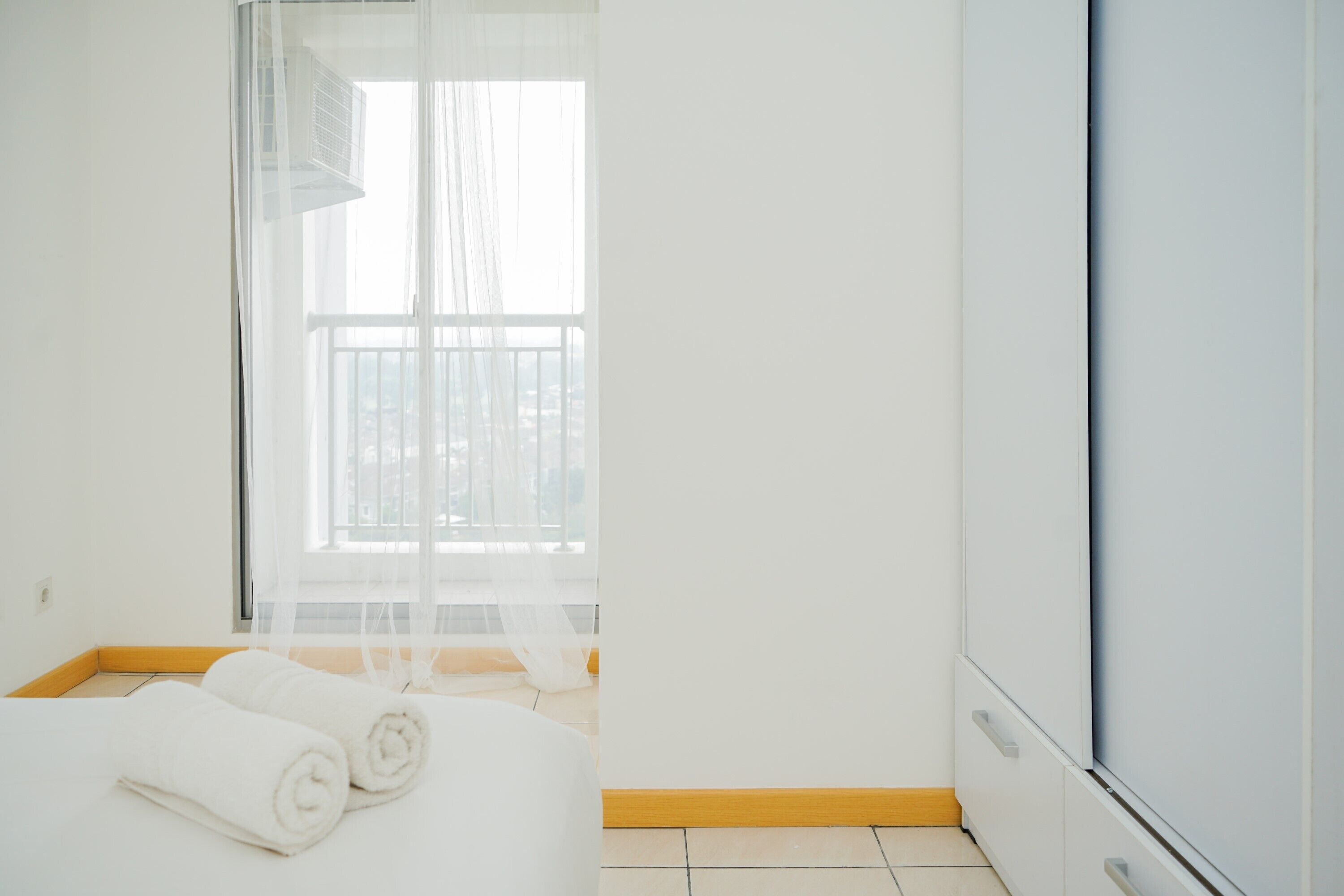 Una habitación de hotel con una cama, un ventanal con cortinas traslúcidas y un armario blanco.