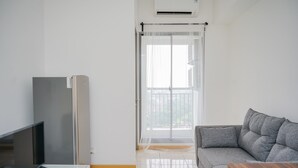 A modern living room with a flat-screen TV, a grey sofa, a wooden coffee table, and a sliding glass door leading to a balcony.
