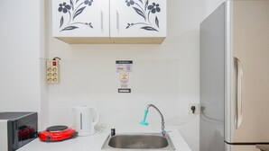 A compact kitchenette with a sink, a red toaster, a kettle, and a refrigerator.