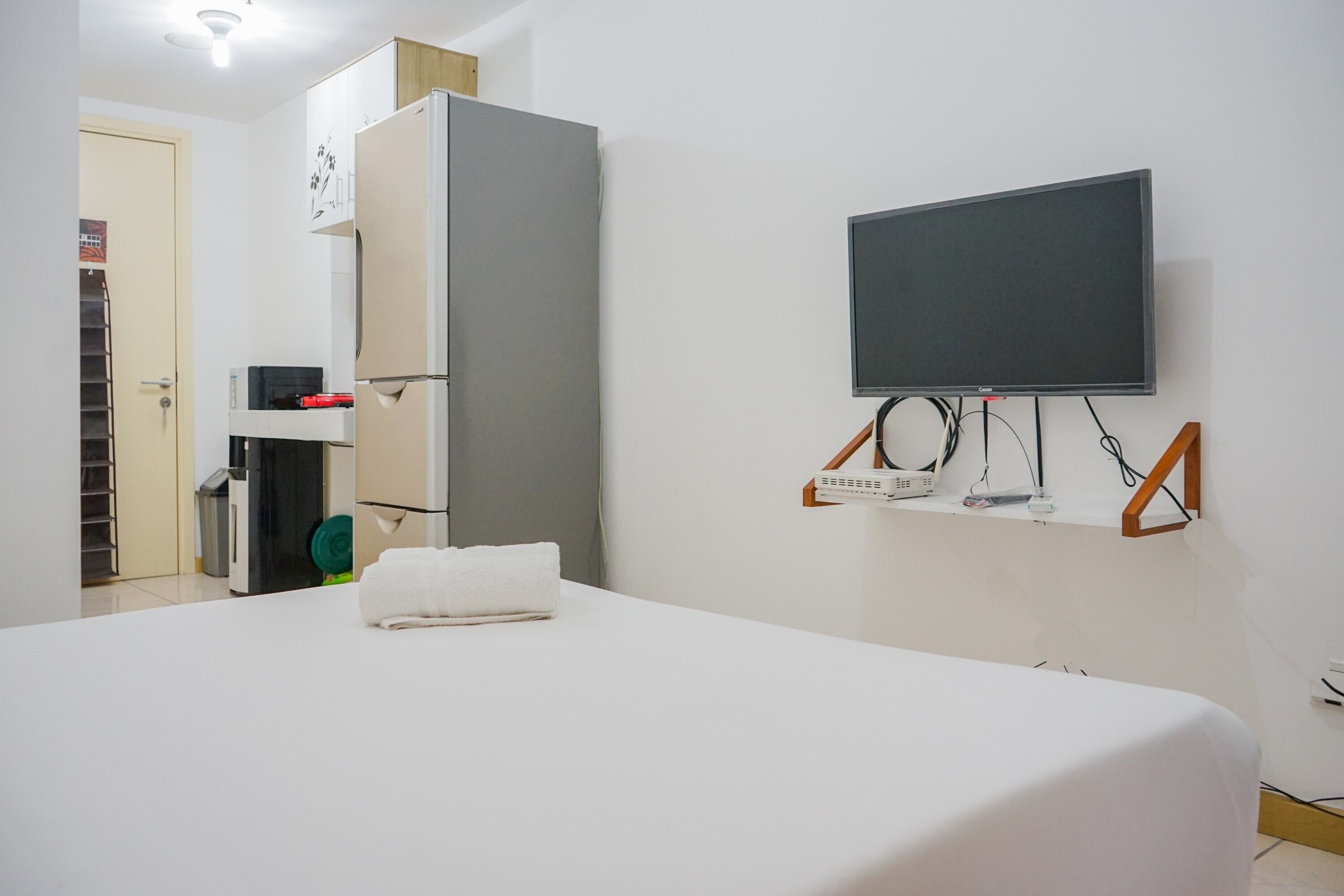 Une chambre d’hôtel comprenant un lit, un téléviseur fixé au mur, une petite étagère avec des appareils électroniques et une armoire.