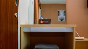 A compact room with a wooden desk, a small black ottoman, a travelio sign, and a laptop on a shelf. - Minimalist and Homey 1BR Grand Kamala Lagoon Apartment (Bekasi)