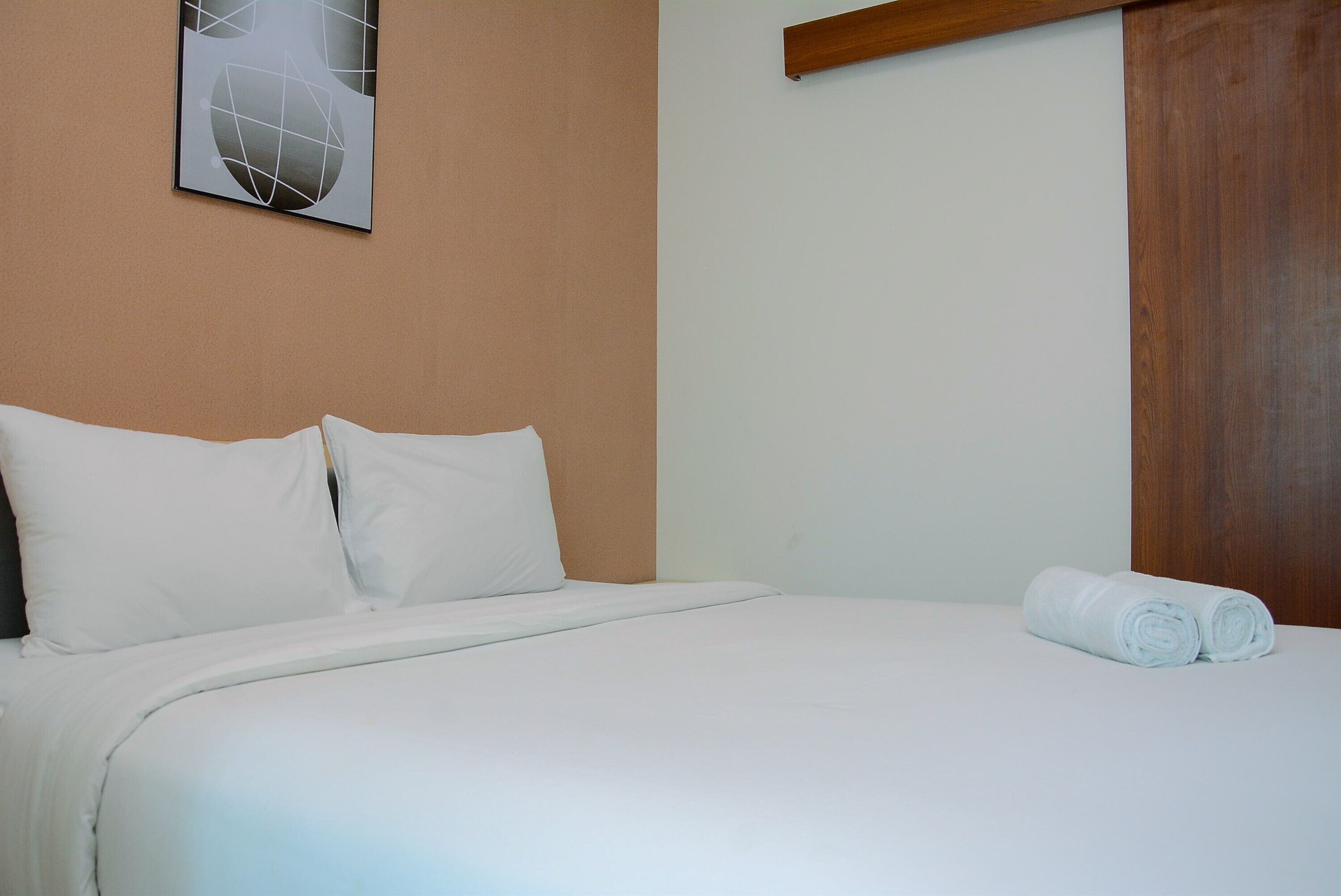 Una cama bien tendida con sábanas blancas, cabecera de madera y una toalla enrollada al lado.