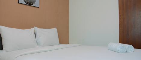 Una cama bien tendida con sábanas blancas, cabecera de madera y una toalla enrollada al lado.