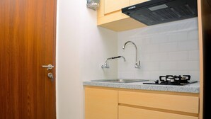 A compact kitchen with a wooden door, a stainless steel sink, a gas stove, and light-colored cabinets. - Minimalist and Homey 1BR Grand Kamala Lagoon Apartment (Bekasi)
