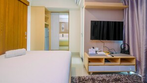 Ein Hotelzimmer mit einem Bett, einem an der Wand befestigten Fernseher, einem Holzschrank und einem kleinen Schreibtisch mit einer Lampe.