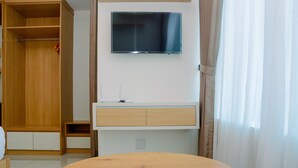Ein Zimmer mit einem Holzschrank, einem flachbildfernseher an der Wand, einem kleinen Holztisch und einem weißen Nachttisch mit Schubladen.