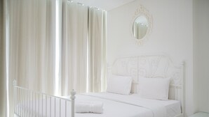 A white four-poster bed with a white headboard, a round mirror above it, and a white nightstand beside the bed. - Cozy Living 1BR at Brooklyn Alam Sutera Apartment (South Tangerang)