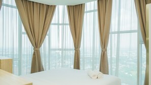 Una habitación de hotel con una cama grande, cortinas color beige y vistas a la ciudad a través de amplios ventanales.