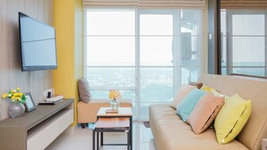 Una sala de estar moderna con un sofá, una mesita, un televisor montado en la pared y grandes ventanales con vistas a la ciudad.