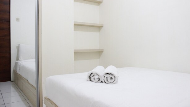 A clean, white hotel room with a neatly made bed, a wooden door, and a white wall with a shelf. - Relaxing 2BR Apartment at Buah Batu Park (Dayeuhkolot)