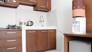 A kitchen with wooden cabinets, a white countertop, a kettle, a coffee maker, and a water dispenser. - Relaxing 2BR Apartment at Buah Batu Park (Dayeuhkolot)