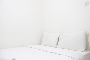 Simple room with a single bed, featuring a white mattress and two pillows.