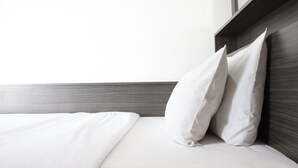 Uma cama bem arrumada com lençóis e almofadas brancas, cabeceira de madeira e parede lisa.