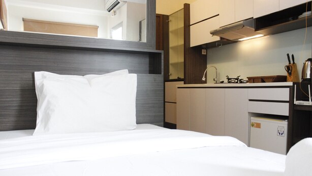 Quarto de hotel com cama, cozinha compacta e um pequeno frigorífico.
