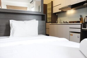 A hotel room with a bed, a kitchenette, and a small refrigerator. - Chic Studio Apartment at Harvard Jatinangor (Cileunyi)