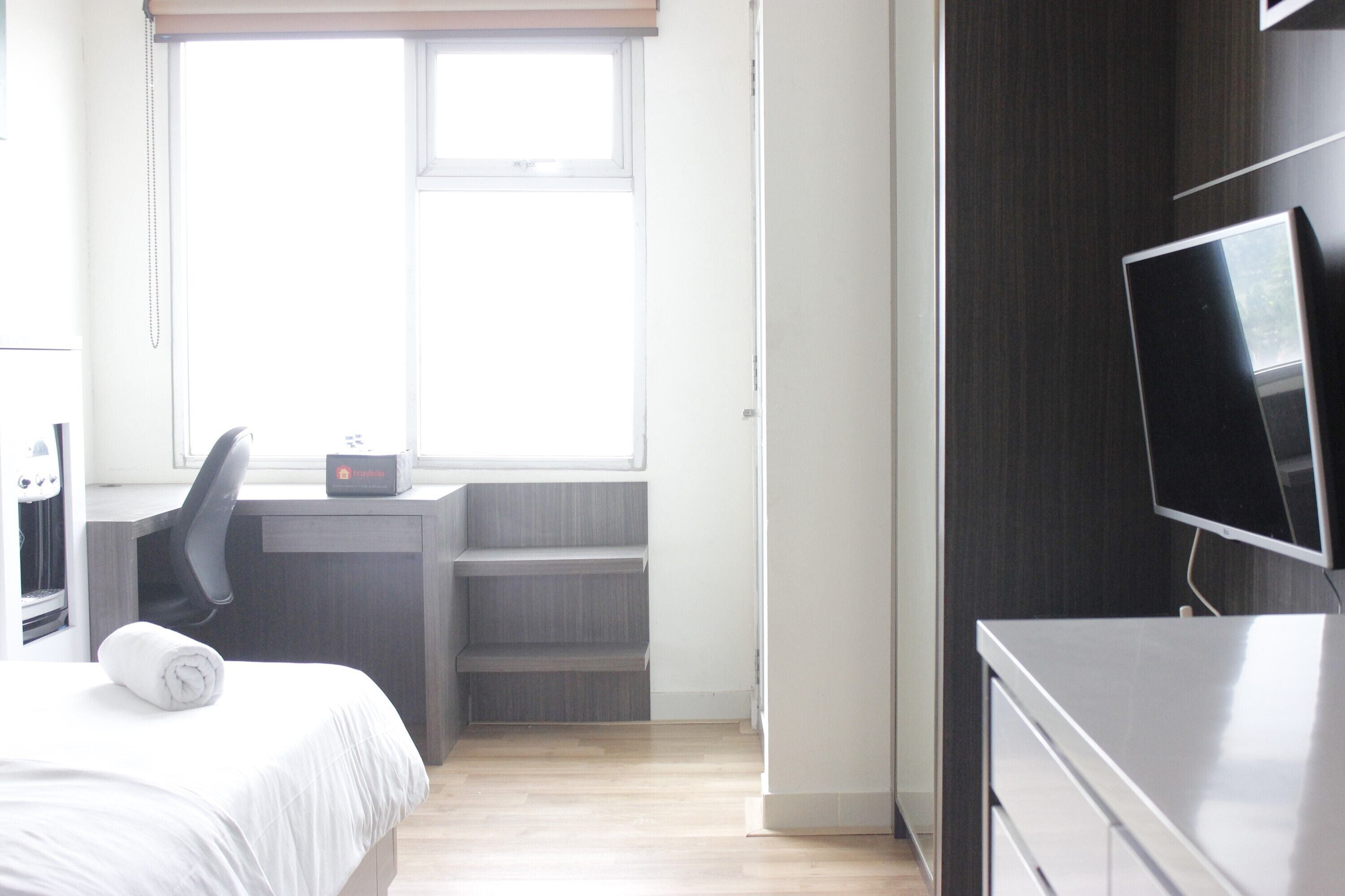 A hotel room with a bed, a desk, a chair, a television, and a window.