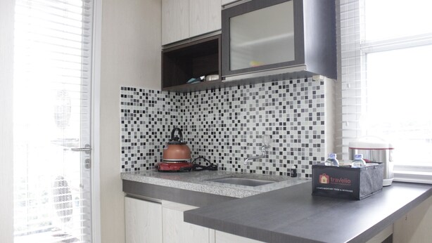A modern kitchen with a tiled backsplash, a kettle, and a box labeled 'travelio' on the counter.