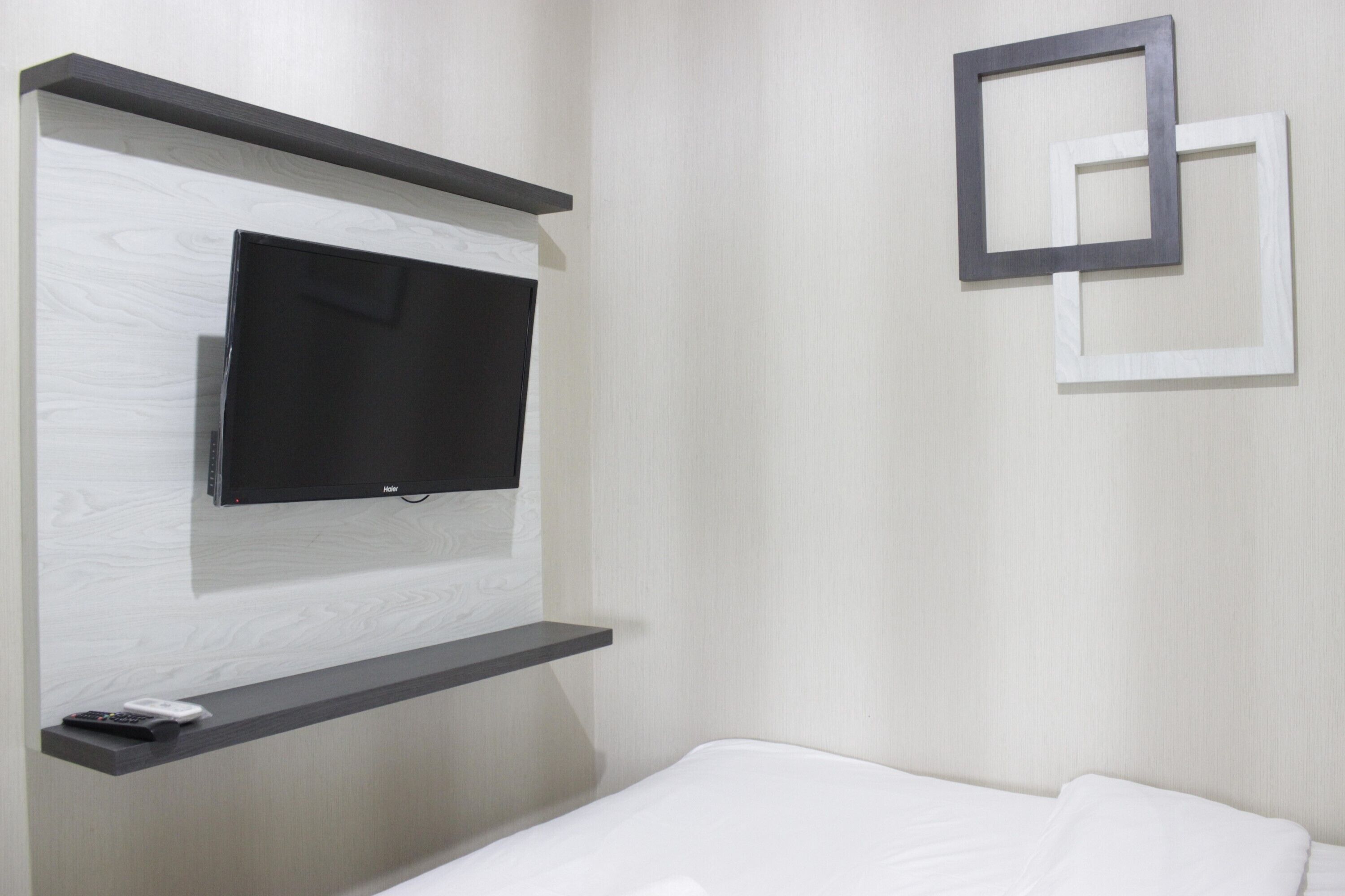 A modern hotel room with a flat-screen TV mounted on a wooden panel, a bedside table, and a bed with white bedding.