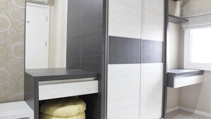 A modern bathroom with a grey and white tiled shower enclosure, a white toilet, and a beige cushioned bench.