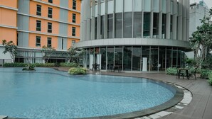 Un edificio moderno con una piscina circular rodeada por una terraza de madera y mobiliario exterior.
