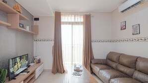 Una sala de estar moderna con un televisor de pantalla plana, un sofá, una mesa de centro y una ventana con cortinas.