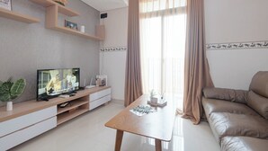 Una sala de estar moderna con un televisor de pantalla plana, una mesa de centro de madera, un sofá color beige y un ventanal con cortinas.