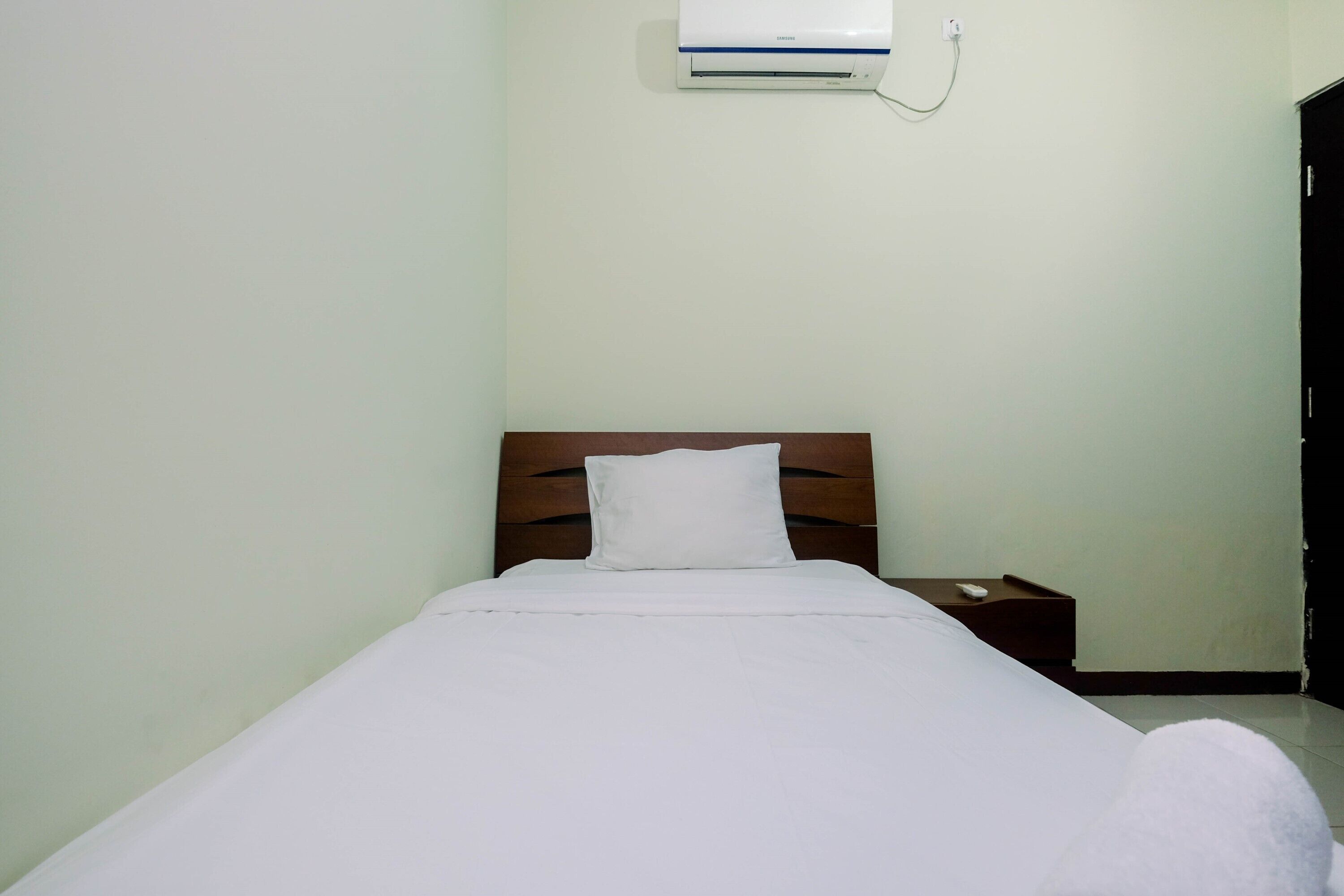 A single bed with a wooden headboard, a white pillow, and a bedside table with a remote control.