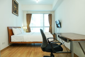 Ein Schlafzimmer mit Bett, Schreibtisch, Stuhl, Fernseher und einem Fenster mit Vorhängen.