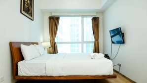 Une chambre d’hôtel moderne avec un lit en bois, du linge de lit blanc, un téléviseur à écran plat et une grande fenêtre avec des rideaux.