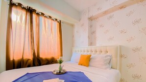 A neatly made bed with a blue bedspread, white pillows, and a decorative vase with flowers. - Relaxing 2BR Bassura City Apartment (Jakarta)