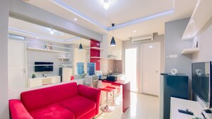 A modern living room with a red sofa, a TV, and a kitchen area with a water dispenser and a small island. - Relaxing 2BR Bassura City Apartment (Jakarta)
