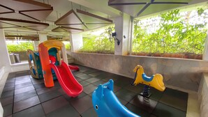 A covered play area with a slide, a rocking horse, and a blue swing set. - Relaxing 2BR Bassura City Apartment (Jakarta)