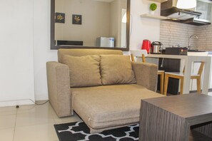A compact living space with a sofa, a small table, and a kitchenette area. - Best View 2BR Apartment at Bassura City (Jakarta)