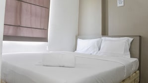A neatly made bed with white linens and pillows, a bedside table with a white towel, and a wall-mounted sign. - Best View 2BR Apartment at Bassura City (Jakarta)