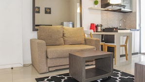 A modern living room with a sofa, a coffee table, and a kitchen area with a sink and stove. - Best View 2BR Apartment at Bassura City (Jakarta)
